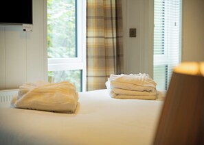 A hotel room with a bed, a television mounted on the wall, and a window with curtains.
