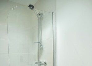 A shower with a handheld showerhead, a vertical rain showerhead, and a glass door.