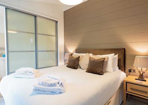A hotel room with a bed, a nightstand, a lamp, and a large window with blinds.