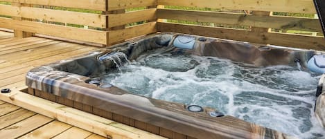 A hot tub on a wooden deck with a wooden fence in the background.