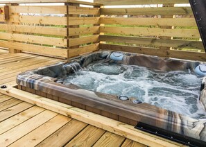 A hot tub on a wooden deck with a wooden fence in the background.