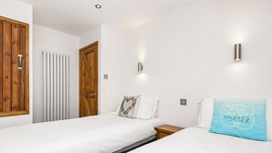 A bedroom with two beds, wooden doors, a radiator, and a wall-mounted light fixture. - Apple Cottage is a firm favourite with our guests. (Watergate, Looe)