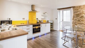 A modern kitchen with white cabinets, a yellow backsplash, and a stone accent wall. - Apple Cottage is a firm favourite with our guests. (Watergate, Looe)