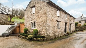 A stone building with a staircase, a wooden door, and a small garden with bushes. - Apple Cottage is a firm favourite with our guests. (Watergate, Looe)