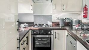 A modern kitchen with white cabinets, a stainless steel oven, a gas stove, and a red fire extinguisher. - Country Lodge Four Spa (Tintagel)