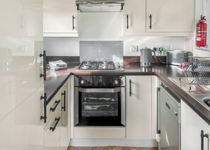 A modern kitchen with white cabinets, a stainless steel oven, a gas stove, and a red fire extinguisher.