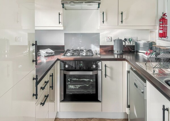 Una cocina moderna con gabinetes blancos, un horno de acero inoxidable, una estufa a gas y un extintor de incendios rojo.