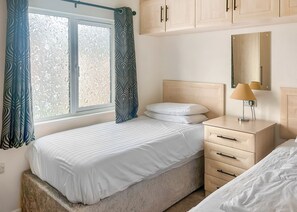 A bedroom with a bed, a nightstand, a lamp, a dresser, and a window with curtains.