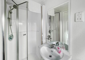 Casa de banho com cabine de chuveiro em vidro, lavatório branco com espelho e placa a indicar 'Shavers Only'.