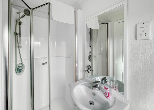 A bathroom with a glass shower enclosure, a white sink with a mirror, and a 'Shavers Only' sign. - Country Lodge Four Spa (Tintagel)