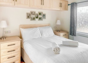 Uma cama bem arrumada com lençóis brancos, uma cabeceira e uma mesa de cabeceira com abajur.
