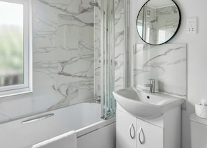 Un baño con cabina de ducha de vidrio, un lavabo blanco y pared con diseño de mármol.