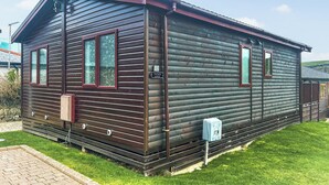 A log cabin with a dark exterior, two windows with red frames, a small porch, and a mailbox. - Country Lodge Four Spa (Tintagel)