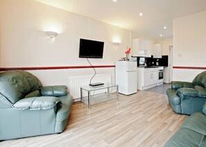 A living room with a sofa, a coffee table, a TV, and a kitchen area with cabinets and appliances.