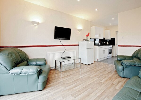 A living room with a sofa, a coffee table, a TV, and a kitchen area with cabinets and appliances.