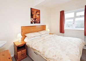 Et soveværelse med en seng, sengeborde, en træsenggavl, et vindue med gardiner og et vægmaleri.