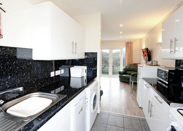 A modern kitchen with granite countertops, a built-in washing machine, and a dining area with a green sofa.