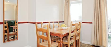 A dining room with a wooden table and chairs, a mirror, and a window with curtains.