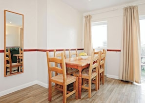 Uma sala de jantar com mesa e cadeiras de madeira, um espelho e uma janela com cortinas.