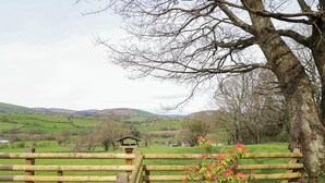 A wooden deck with a view of rolling hills and a distant village. - The Retreat (Oswestry)