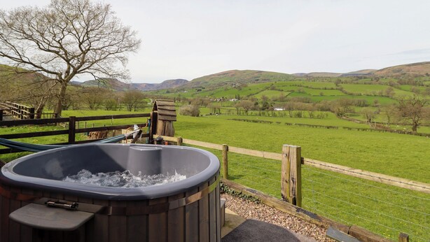 A hot tub with a wooden deck and a view of rolling hills and a clear sky. - The Retreat (Oswestry)