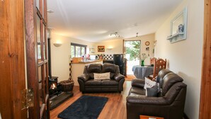 A cozy living room with two leather sofas, a dark rug, and a wooden coffee table. A kitchen area is visible in the background with a refrigerator and a sink. - The Retreat (Oswestry)