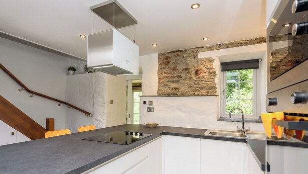 Une cuisine moderne avec un mur d’accent en pierre, une cuisinière intégrée et une fenêtre donnant sur un espace verdoyant.