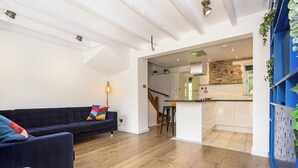 Un intérieur moderne avec un canapé bleu foncé, une petite table blanche et un coin cuisine doté de meubles blancs et d’un mur d’accent bleu.