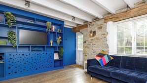 Un salon moderne avec un meuble de rangement bleu, un canapé bleu foncé, un plancher en bois et un mur en pierre.