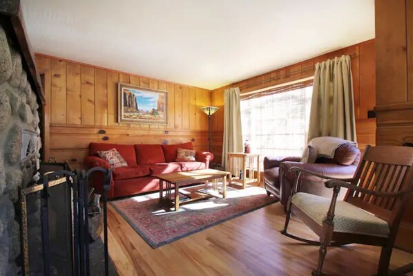 A cozy living room with wooden walls, a red sofa, a wooden coffee table, and a wooden chair.