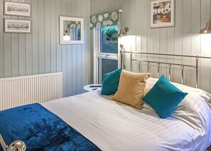 A bedroom with a bed, pillows, a bedside table, a lamp, and framed pictures on the wall.