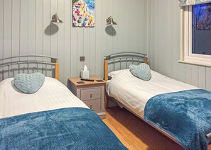 A room with two beds, each with a heart-shaped pillow, a bedside table with a remote control, a tissue box, and a wall-mounted light fixture. - 2 bedroom accommodation in Easingwold (Easingwold)