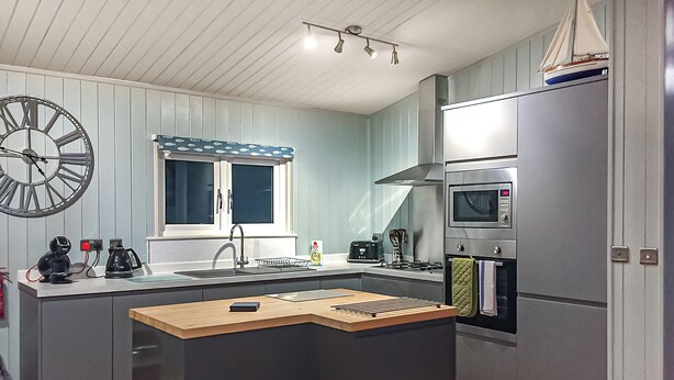 Une cuisine compacte dotée d’un îlot central, d’un four à micro-ondes encastré et d’une fenêtre ornée d’un rideau bleu.