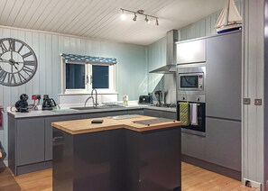 A compact kitchen with a central island, a built-in microwave, and a window with a blue curtain.