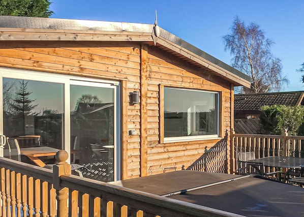 A wooden cabin with a deck, a sliding glass door, and a small outdoor table. - 2 bedroom accommodation in Easingwold (Easingwold)