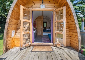 Une cabane en bois avec une porte centrale donnant sur une chambre à coucher équipée d’un lit et d’une fenêtre.