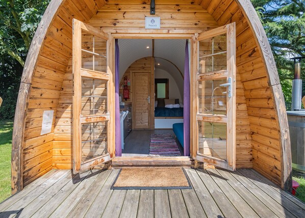 A wooden cabin with a central door leading to a bedroom with a bed and a window.