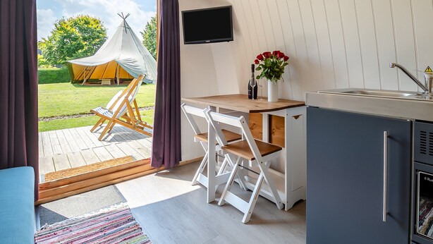 Eine kompakte Küche mit Spüle, Flachbildfernseher und kleinem Kühlschrank.
