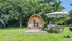 Eine Holzhütte mit einer Terrasse, zwei Liegestühlen, einem Tisch und einem Grill.