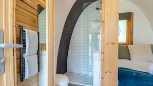 Ein kleines, modernes Badezimmer mit Dusche, Toilette und Waschbecken, verbunden mit einem Schlafzimmer mit Bett und Fenster.