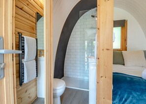 Ein kleines, modernes Badezimmer mit Dusche, Toilette und Waschbecken, verbunden mit einem Schlafzimmer mit Bett und Fenster.