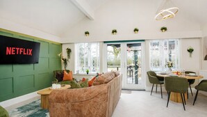 A modern living room with a green accent wall, a leather sofa, a dining area with a table and chairs, and a flat-screen TV mounted on the wall.