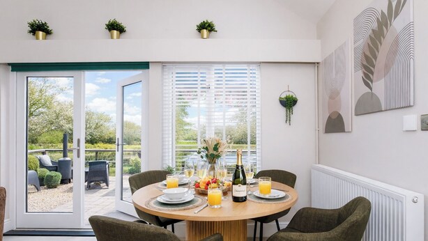A dining area with a round table, four chairs, a bottle of champagne, and a view of the outdoors.