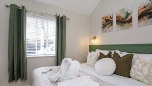 A hotel room with a bed, green curtains, a window with blinds, a headboard, and wall art.