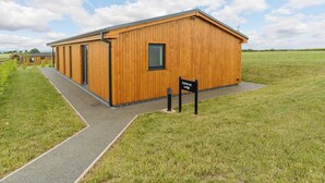A wooden lodge with a paved walkway and a sign indicating its name. - New in 2022 Luxurious and contemporary lodge with stunning countryside views. (Bretby, Derbyshire)