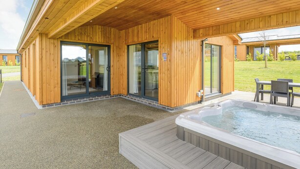 A wooden building with glass doors, a patio area, and a hot tub. - New in 2022 Luxurious and contemporary lodge with stunning countryside views. (Bretby, Derbyshire)