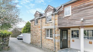 Une maison en pierre à deux étages, avec une extension en bois, une allée gravillonnée et une voiture garée au fond.