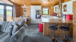 A cozy cabin-style kitchen with wooden walls, a dining area with a table and chairs, a bar with stools, and a view of the outdoors. - Comfortable and spacious lodge with two doubles and one with bunks. (Glenluce, Newton Stewart)