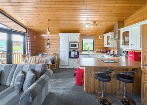 A cozy cabin-style kitchen with wooden walls, a dining area with a table and chairs, a bar with stools, and a view of the outdoors. - Comfortable and spacious lodge with two doubles and one with bunks. (Glenluce, Newton Stewart)
