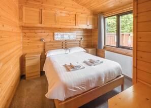 Une chambre à coucher dans une cabane en bois, avec un lit, des tables de chevet, une fenêtre et une horloge fixée au mur.